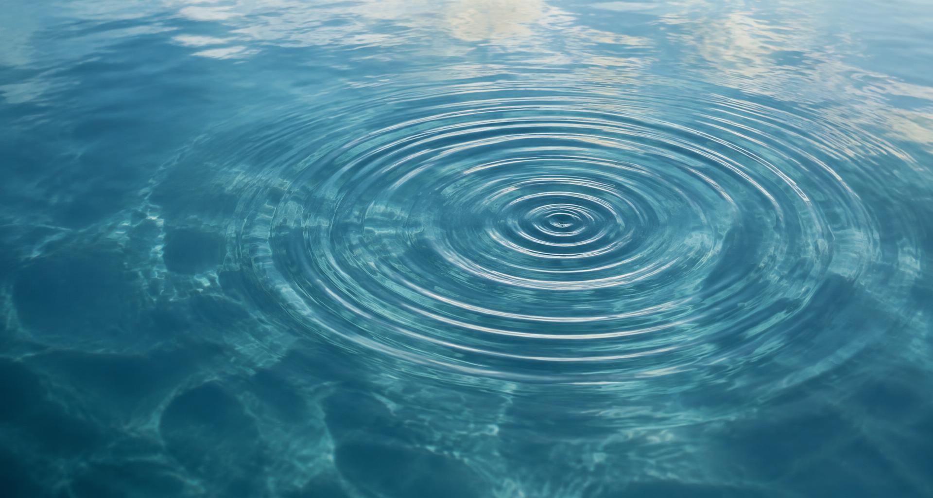 Konzentrische Wellenringe auf einer ruhigen türkisfarbenen Wasseroberfläche, von oben gesehen